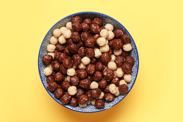 Bowl with tasty chocolate corn balls on yellow background, closeup