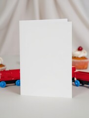 Blank White Greeting Card with Red and Blue Train Toys and Cupcakes in Soft Bakery Background