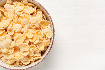 Bowl with tasty cornflakes on white wooden background, closeup