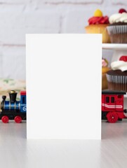 Blank White Greeting Card with Red and Blue Train Toys and Cupcakes in Soft Bakery Background