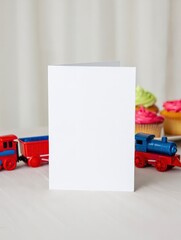 Blank White Greeting Card with Red and Blue Train Toys and Cupcakes in Soft Bakery Background