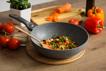 Frying pan with tasty vegetables and wooden spoon on counter in kitchen, closeup