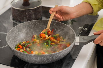 Woman with spoon frying vegetables on stove in kitchen, closeup