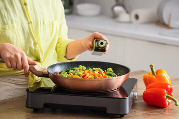 Woman with olive oil frying vegetables on mini stove in kitchen, closeup