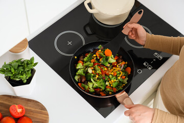 Woman with spatula frying vegetables in kitchen, top view