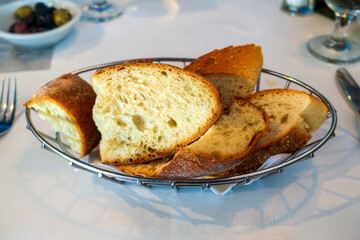 A metal basket holds slices of rustic artisan bread with a golden crust and airy, fluffy interior, perfect for dipping or pairing with olive oil, butter, or a Mediterranean starter.
