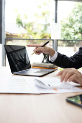 Fototapeta premium A man in a suit is sitting at a desk with a laptop and a calculator. He is holding a piece of paper and he is working on some financial documents. Concept of professionalism and focus 