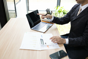 A man in a suit is sitting at a desk with a laptop and a calculator. He is holding a piece of paper and he is working on some financial documents. Concept of professionalism and focus
