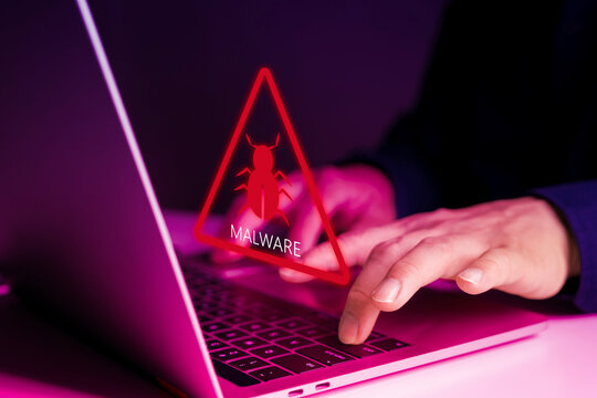 Cybersecurity warning concept showing malware alert symbol on laptop with hacker or user typing in dark room