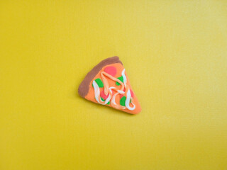 Colorful fake pizza slice from plasticine clay isolated on yellow background. Artificial food concept