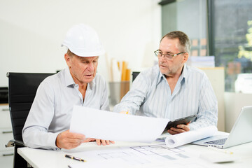 Engineers planning a construction project with blueprints, tablets, and hardhats. Concept of teamwork, architecture