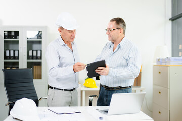Construction engineers reviewing blueprints and tablet at desk. Team collaboration and planning for architecture or renovation project