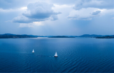 Two Sailboats on Sea with Distant Mountains and Clouds