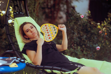 Woman Sitting on a Garden Lounger and Fans Herself. Person unwell from heat wave tries to relax outside 