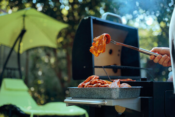 Person Holds Fresh Barbecue Meat with a Fork. Amateur chef relaxes at a grill session in the garden  
