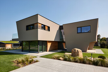 Modern angular house with green roof and stone landscaping under a clear sky