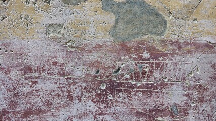 Pompeii between the theatres, Italy - 8 January 2025. Uneven red and yellow plaster wall scratched with names, boxes and lines, patched with mortar.