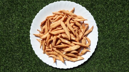 Top view of crispy golden namakpara or nimki, a traditional deep-fried Indian savoury snacks served mostly during Diwali festival or tea time snacks in white plate on green grass background