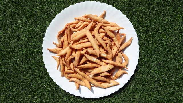 Top view of crispy golden namakpara or nimki, a traditional deep-fried Indian savoury snacks served mostly during Diwali festival or tea time snacks in white plate on green grass background