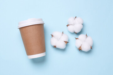 Disposable cardboard coffee cup and cotton flowers on blue background
