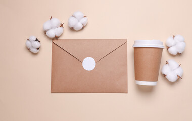 Kraft envelope with white blank sticker and cardboard coffee cup, cotton flowers on beige background. Top view