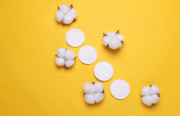 Cotton pads for makeup and cotton flowers on yellow background. Top view