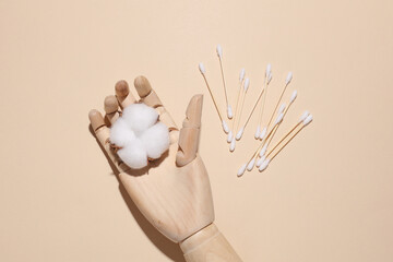 Wooden puppet hand holding cotton flower and Cotton swabs on beige background. Self care