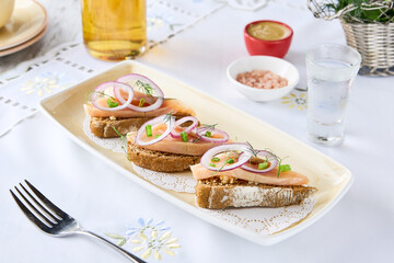 Herring toast with onions, bright overhead, minimalist presentation on embroidered tablecloth