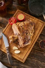 Bone-in roasted meat rustic bright overhead with wooden board, garlic, sauces, and side spices