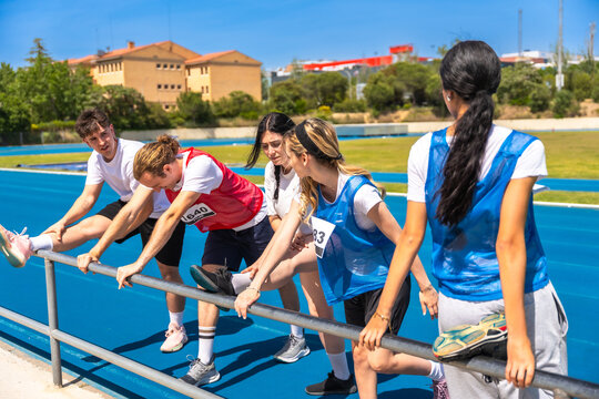 Athletes stretching legs on track and field railing