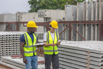 Two civil engineers from different ethnicities and genders working together using tablet, smartphone, and walkie talkie to check the quality of precast products in a construction factory