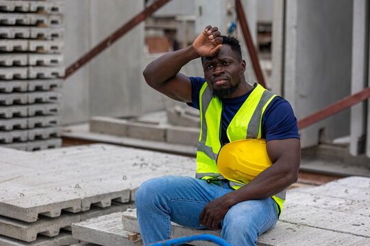 African constructer or civil engineer expresses his exhausted moment next to precast cement floors or slabs. Black worker sits in a construction factory taking rest. Break time in a construction site