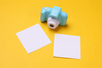 Toy plastic camera with blank cards on yellow background