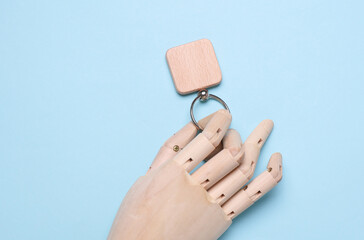 Puppet hand holding wooden keychain on blue background