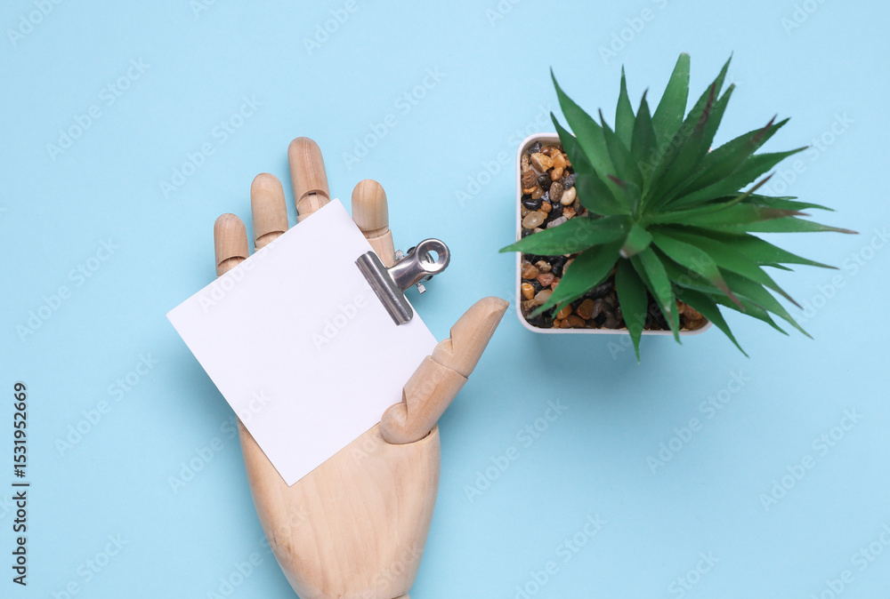 Poster wooden hand of puppet holding square memo card with binder on blue background