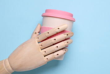 Wooden puppet hand holding eco plastic coffee cup on blue background