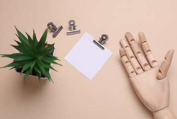 Wooden hand of puppet and square memo card with metal binders on beige background. Business concept