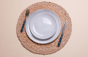 Example of aesthetic table setting. Straw woven rug with plate and cutlery on beige background