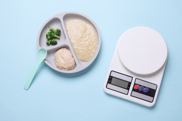 Baby food divider plate with healthy food and kitchen scales on blue background