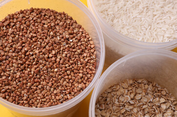 Plastic jars with buckwheat, oatmea and rice on yellow background. Top view