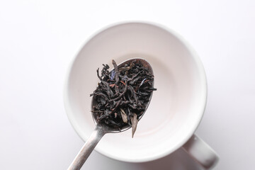 Black tea leaves in spoon on cup background.