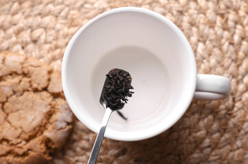 Black tea leaves in spoon on cup background.