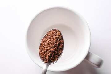 Instant coffee granules in a spoon against a cup background.