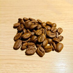 A close-up shot of roasted coffee beans arranged in a shape on a light wooden table