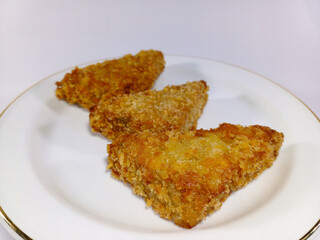 Close-up of three pieces of golden-brown soun goreng, a type of fried noodle or vermicelli dish, arranged on a white plate with a gold rim against a white background, indicative of a savory dish