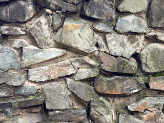 Texture of an old stone wall made of rough rocks with moss and cracks. Natural stone background.