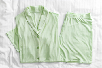 Top view of folded pastel green pajama set on white bed. Minimal style, cozy, and comfort pyjamas. Sleepwear fashion concepts, selfcare, wellness, calm lifestyle, home aesthetics, or morning routines