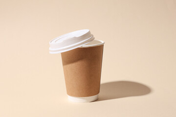 Craft cardboard disposable coffee cup on beige background with shadow. Minimalistic scene