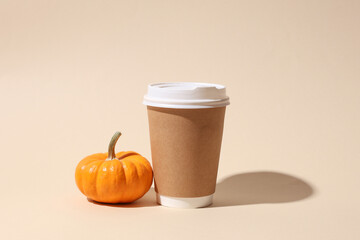 Craft cardboard disposable coffee cup and pumpkin on beige background with shadow. Minimalistic scene
