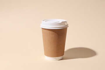Craft cardboard disposable coffee cup on beige background with shadow. Minimalistic scene
